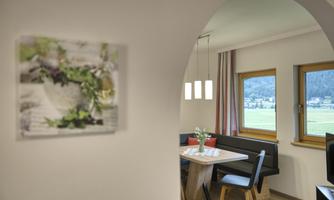 A bright dining room with a table and modern chairs. A piece of artwork hangs on the wall and large windows offer a view of the landscape.