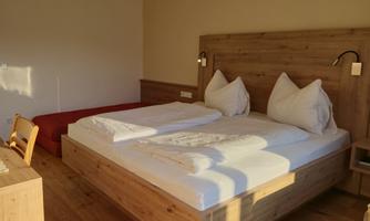 A modern bedroom with a large double bed and two pillows. The room has a warm wood look and plenty of daylight.