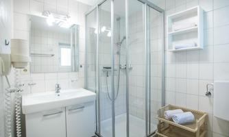 A modern bathroom with a walk-in shower and a sink. White tiled walls and a wicker laundry basket complement the renovated atmosphere.