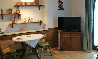 A cozy room with a table and chairs.  
On the wall, there are shelves with decorations, and a television stands in the corner.