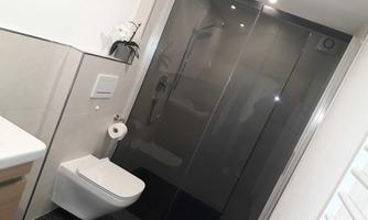 A modern bathroom with a clear shower cabin and an elegant toilet seat. The walls are in neutral tones and provide a contemporary atmosphere.