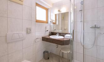 A modern bathroom with a shower and a sink. It has bright tiles and a window that lets in natural light.