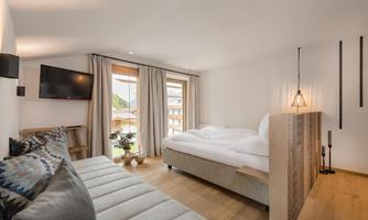 A modern bedroom with a large bed and a cozy sofa. Large windows let in plenty of daylight and provide a view outside.