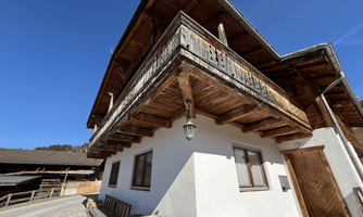 A traditional alpine house with a large wooden balcony. The clear blue sky complements the rural atmosphere.