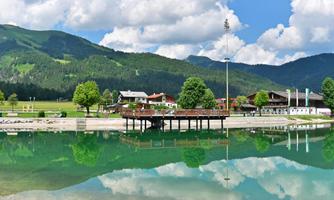 A beautiful lake with green water and a serene shoreline. In the background, mountains and clouds can be seen.