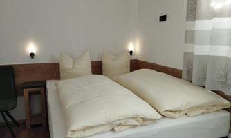 A cozy bedroom with a large bed and two pillows. The walls are light, and the room has a pleasant, modern atmosphere.