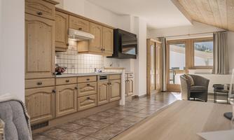 A cozy kitchen with wooden cabinets and modern appliances. The room is bright and inviting, with access to a balcony.
