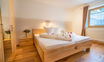 A cozy bedroom with a large bed and wooden furniture. On the bed lies a pillow and a vase with flowers.