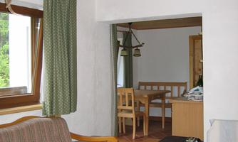 A cozy living space with a sofa and a wooden table. In the background, the dining area with chairs and a window can be seen.