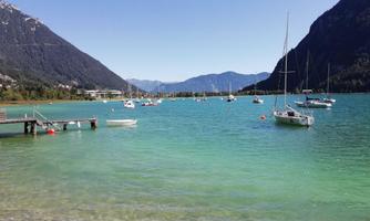 A beautiful lake surrounded by mountains with sailing boats. The water has a clear turquoise color and the sun is shining.