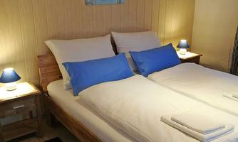A cozy bedroom with a double bed and blue pillows. The walls are light, and there is a piece of artwork as well as bedside lamps.