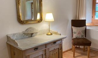 A rustic wooden cabinet with a marble top stands against the wall. Next to it is a chair and a lamp provides warm light in the room.