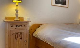 A cozy bedroom with a large bed and a wooden nightstand. The lamp provides warm light, and there is a decorative picture on the wall.