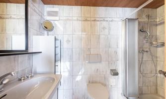 A modern bathroom with a shower and a sink. The walls are tiled and the floor has a wooden covering.