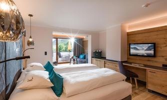 A modern hotel room with two beds, wooden paneling, and a television. The windows offer a view of nature.