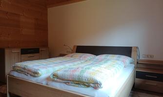 A cozy bedroom with a large double bed and colorful comforters. The walls are made of wood, and there are modern furniture pieces.