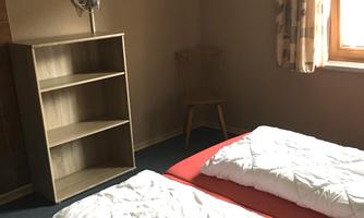 A simple room with two single beds and bright bedding. The room has a window with a view and a shelf.