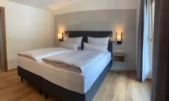 A comfortable bedroom with a large double bed and bright walls. The room has wooden flooring and plenty of daylight.