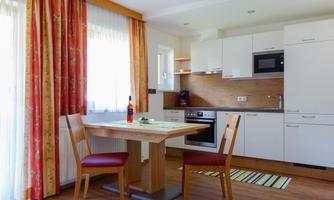 A modern kitchen with bright wood design and white cabinets. The table is decorated with two chairs and a bottle of wine.