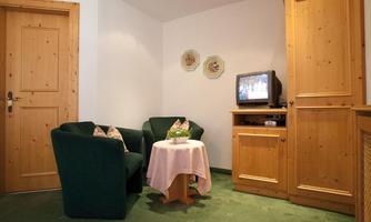 A cozy living area with two green armchairs and a small table. A television and a wooden cabinet are located on the wall.