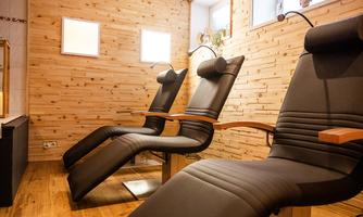 A relaxing room with two comfortable lounge chairs. The walls are made of wood and there are large windows that provide natural light.