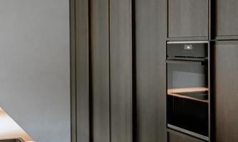 A modern kitchen with elegant dark wooden cabinets and a built-in oven. The furniture is simply and stylishly designed.