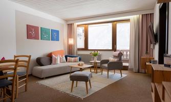 A cozy living room with a modern sofa and a small table. Large windows offer a view of the mountains and let in plenty of light.