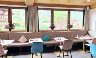A cozy café with large windows and a view of the greenery. The furniture is modern and colorful.