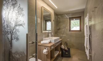 A modern bathroom with a shower cabin and a wooden washbasin. The walls are in neutral tones, and there is a large window for natural light.