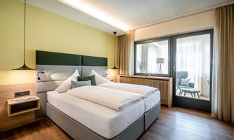 A modern bedroom with a cozy double bed and bright walls. Large windows allow for plenty of daylight and offer a view of the outdoor area.