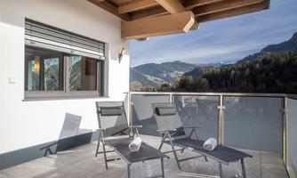 A modern balcony with several loungers and a view of the mountains. The surroundings are bright and inviting, ideal for relaxing.