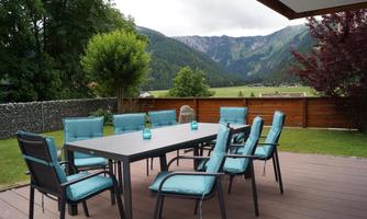 A beautiful outdoor area with a large table and chairs. In the background, the mountains and a green landscape can be seen.