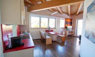 A modern kitchen with a dining area and large windows that let in plenty of light. The space has a bright, cheerful atmosphere.
