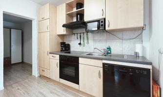 A modern kitchen with bright wooden cabinets and black appliances. It is well-equipped and has plenty of space for meal preparation.