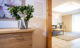 A bright room with a modern sofa and a rug. A plant in a vase stands on a wooden table next to a wall with a picture.