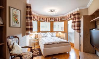 A cozy bedroom with a large bed and a table.  
Large windows provide plenty of daylight and an inviting atmosphere.