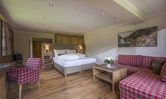 A cozy hotel room with modern furniture and wooden floors. The furnishings consist of a double bed and a living area with seating in an elegant design.