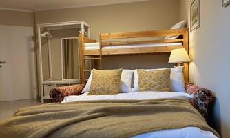 A cozy bedroom with a double bed and a bunk bed. The walls are in neutral colors, and there is a lamp as well as a wardrobe.
