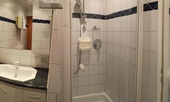 A modern bathroom with a shower, sink, and toilet. The walls are tiled and the furnishings are bright and functional.