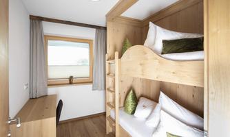 A cozy room with a wooden bunk bed. The window offers a view outside, and there is a desk area.