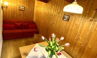 A cozy room with wooden walls, a red sofa, and a table with fresh tulips. The lighting creates a warm, inviting atmosphere.