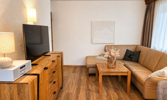 A cozy living room with a beige couch and a wooden table. A television and a lamp blend harmoniously into the furnishings.