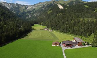 A picturesque landscape with expansive green meadows and wooded mountains. In the foreground, a rustic farmhouse is visible.