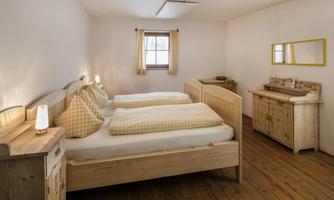 A cozy bedroom with two single beds and wooden furniture. The room has warm colors and windows with curtains.
