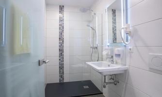 A modern bathroom with a shower and a sink. The walls are light and adorned with stylish tiles.