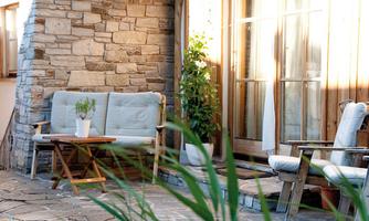 A cozy outdoor area with a stone wall and wooden seating area. A table with a plant and chairs invites you to relax.