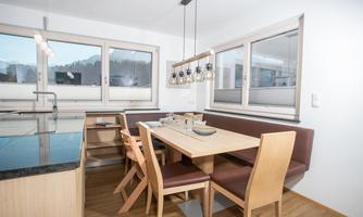 A modern kitchen with a dining area and wooden chairs. Large windows provide plenty of daylight and offer a beautiful view.