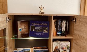 A wooden box with different games and books. A clock is hanging on the wall and a small figure is standing on the shelf.