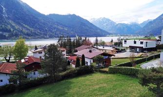 A picturesque landscape with mountains in the background and a calm lake. Small houses with red roofs and green meadows create an idyllic atmosphere.