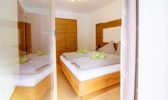 A cozy bedroom with wooden furniture and a large bed. There are fresh green decorations on the pillows and a mirror that expands the space.